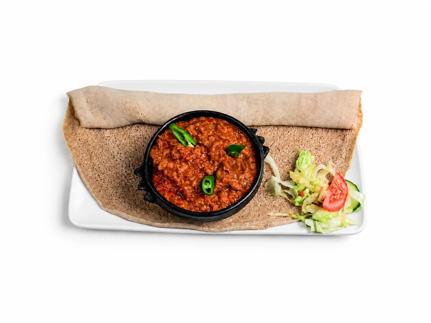 Red lentils in a black bowl with salad and injera
