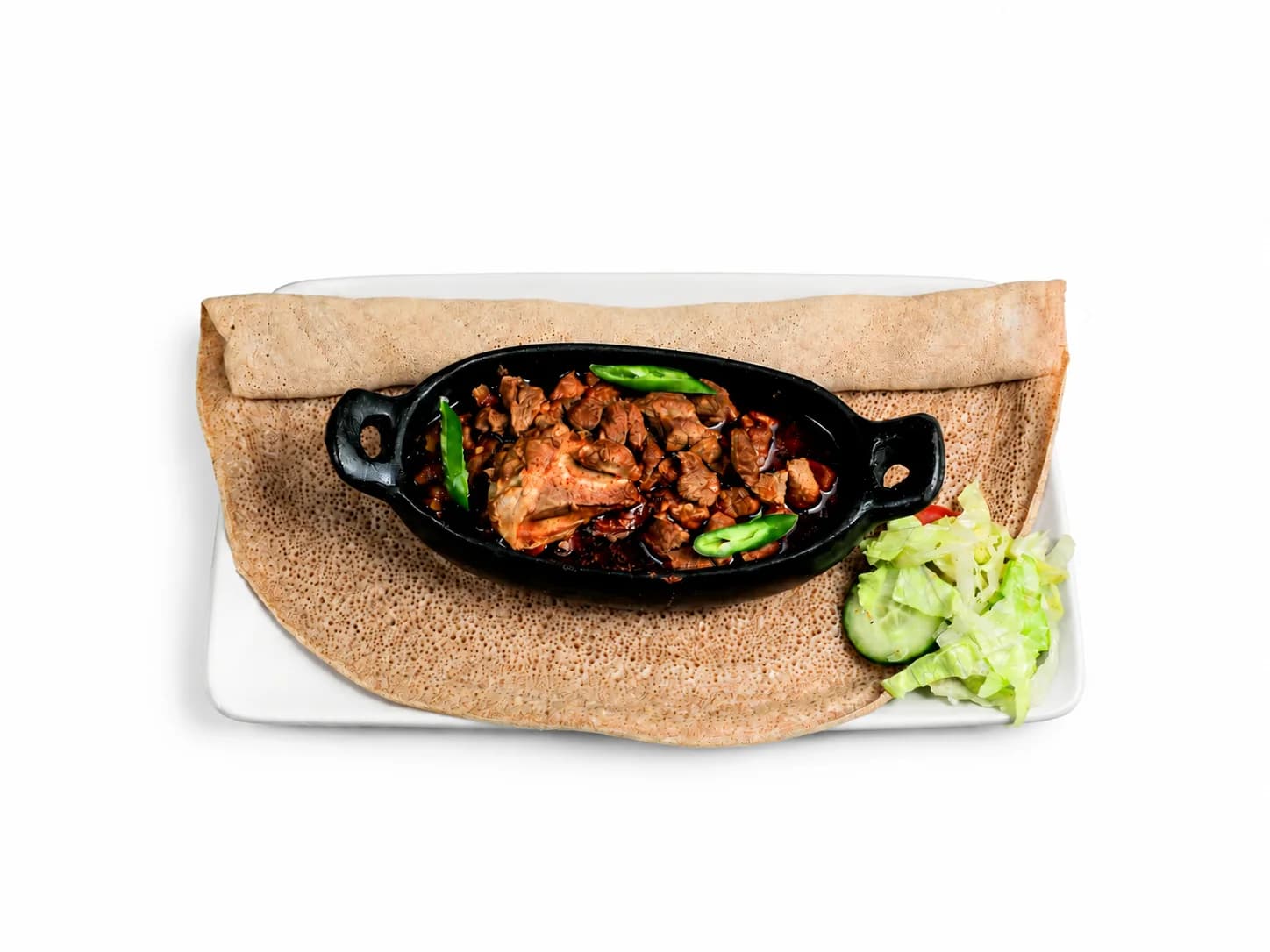 Key Tibs in einer schwarzen Pfanne mit grüner Chili und Injera